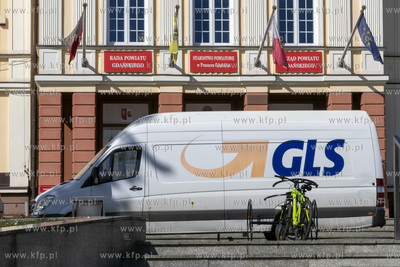 Samochód firmy kurierskiej GLS stoi przed budynkiem...