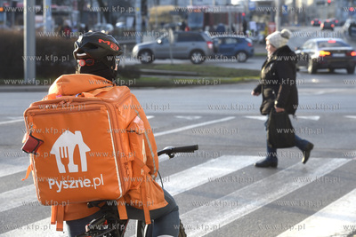 Kurier serwisu pyszne.pl stoi przed przejściem dla...