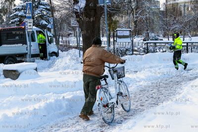 Rowerzysta prowadzący rower przez ośnieżony chodnik...